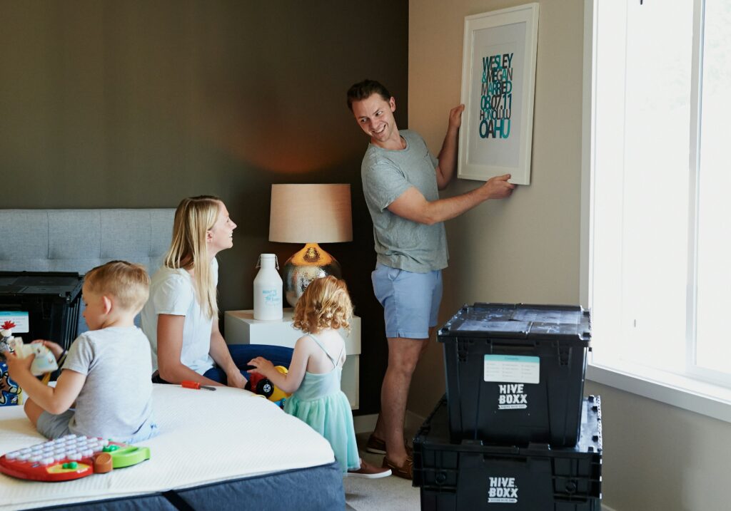 A family hanging a picture on the wall of a home, moving boxes nearby
