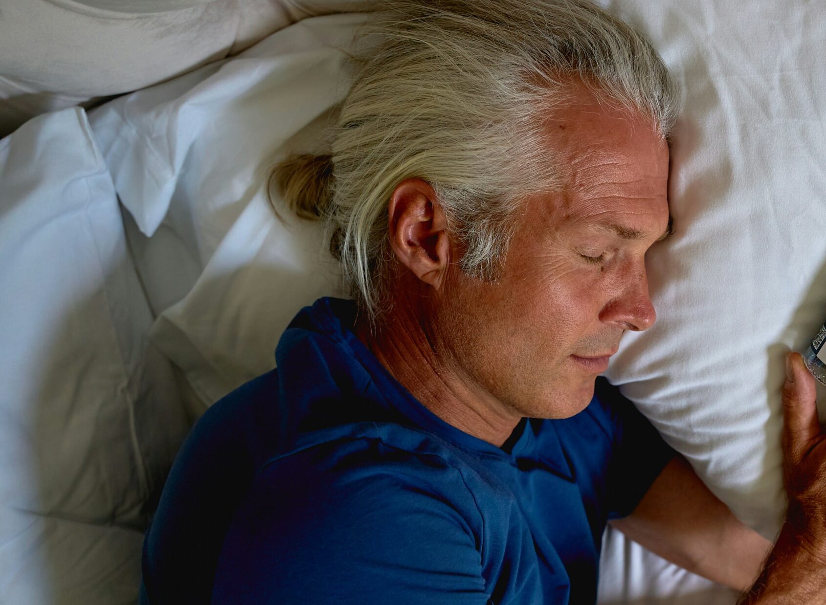An older man asleep on his side in bed, one hand resting near the pillow