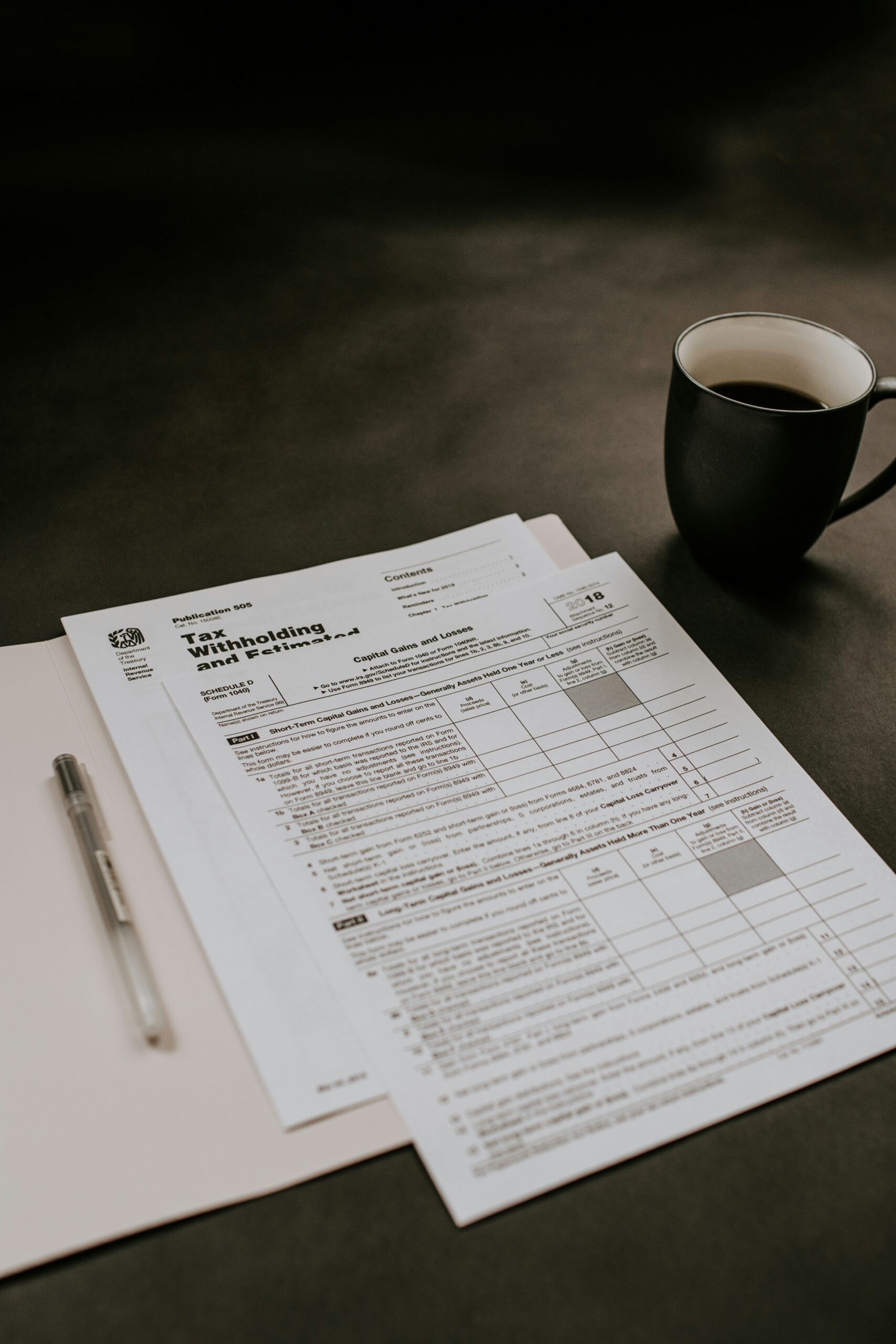 Tax forms, a pen, and a cup of coffee on a desk