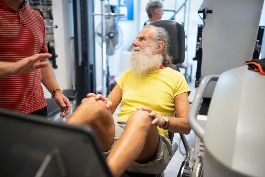 A trainer assisting an older man using a leg press machine