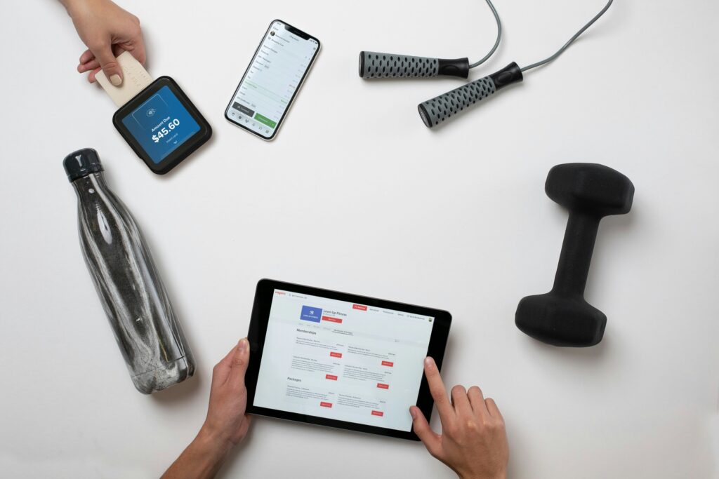 A dumbbell, jump rope, water bottle and tablet arranged on a white table