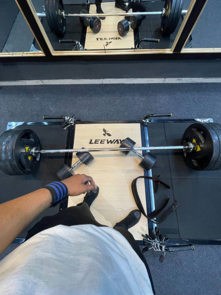 A hand writing in a training notebook beside a loaded barbell
